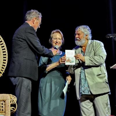 wethouder Michiel van den Busken van gemeente Bergen en voorzitter Joke Volkers van actiegroep Schoorlse Bos moet Blijven ontvangen de eerste exemplaren van Hier is zon, zee en zand uit handen van Kees de Bakker  - foto Peter H. Toxopeus